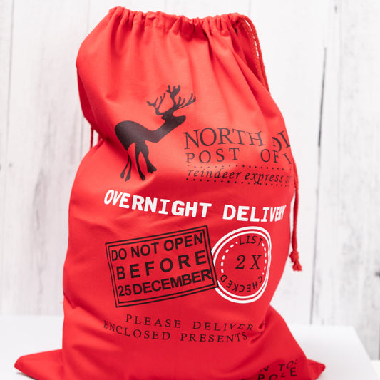 Christmas Gift Bags | Reusable Oversized Fabric with Drawstring Cord - North Pole Post Office Overnight Delivery Logo